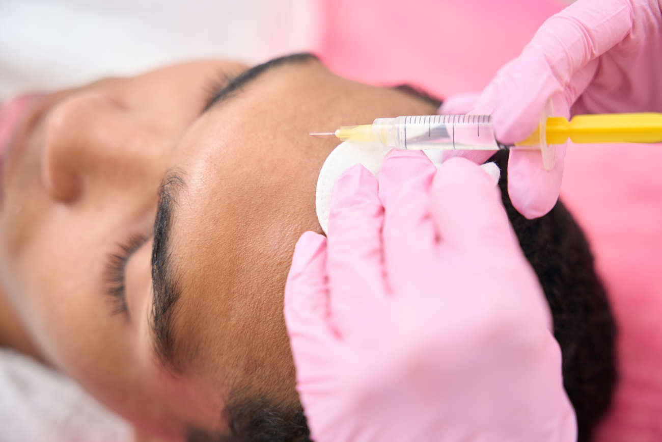 Closeup of young male patient undergoing mesotherapy procedure conducted by qualified dermatologist in nitrile gloves